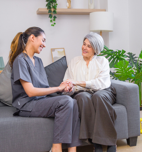 Aged care worker provides comfort and support to a senior woman by holding her hands while sitting together on a sofa